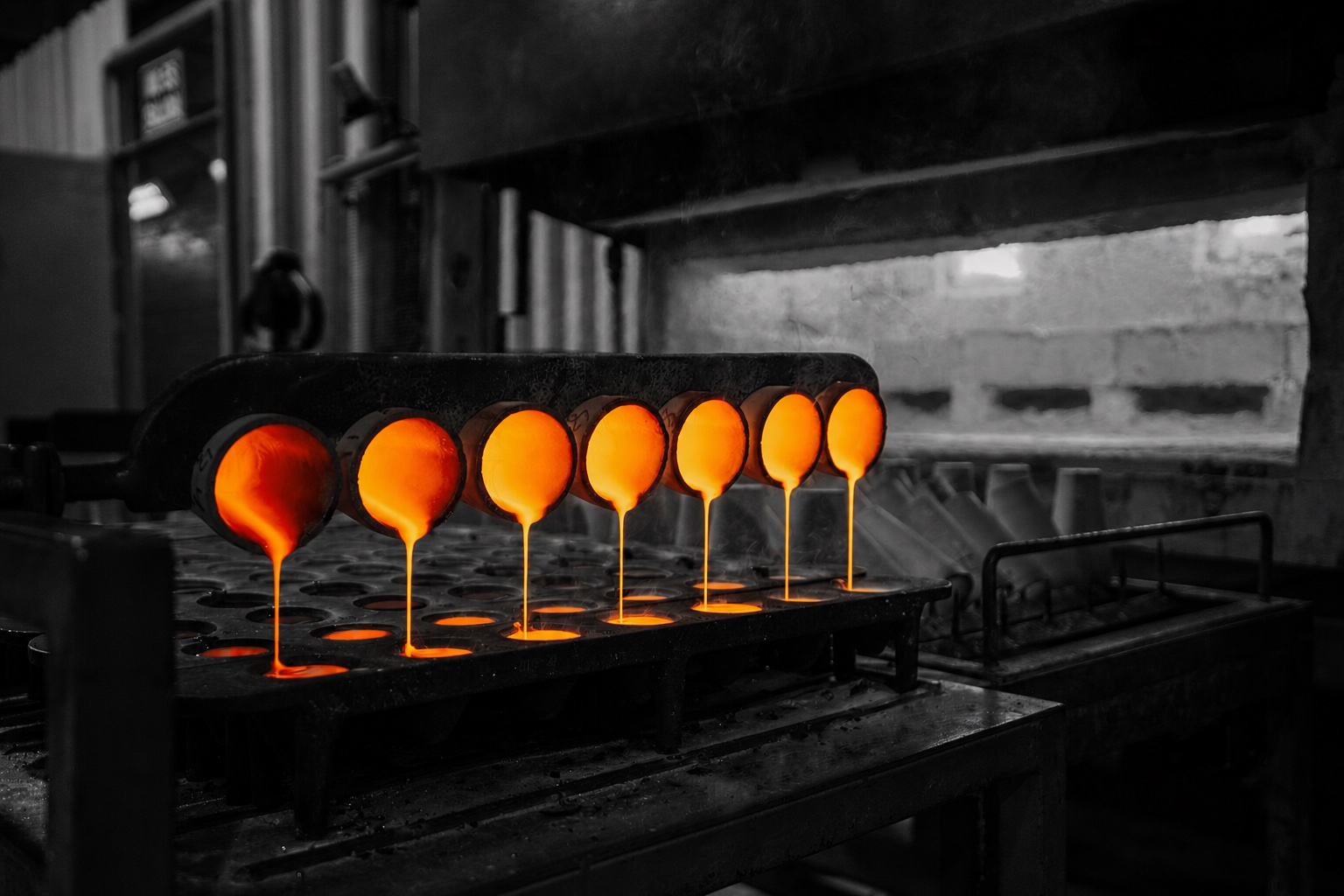 A row of crucibles pouring molten fire-assay fusions into a mold tray in the Eastern Analytical furnace room